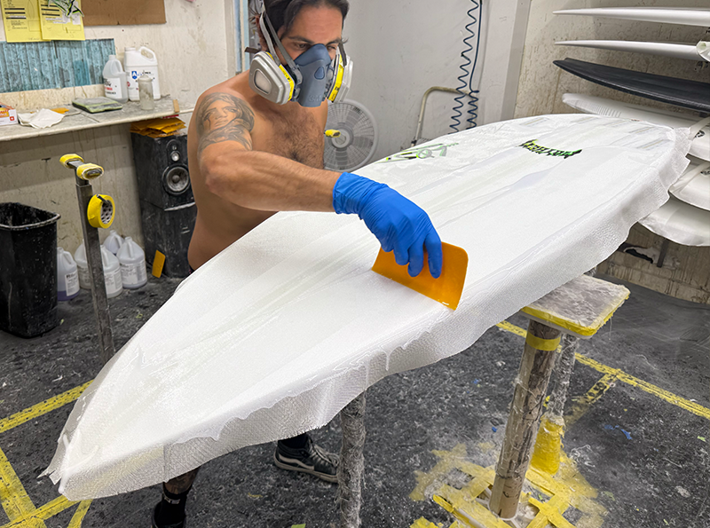 Man shaping a surfboard in a workshop.
