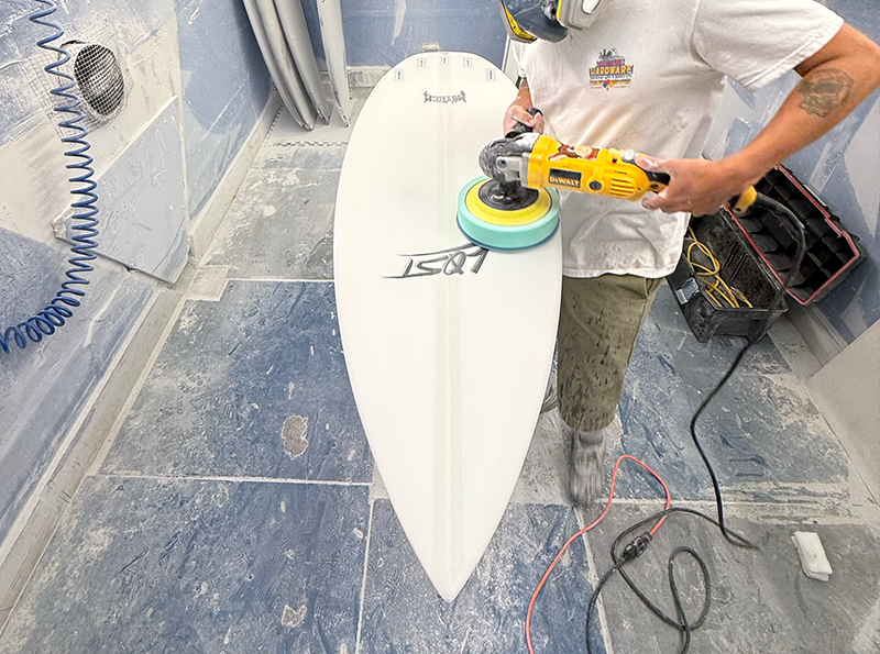 Person polishing a surfboard in a workshop.