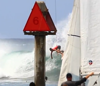 Surfer performing a maneuver near a buoy and sailboat.
