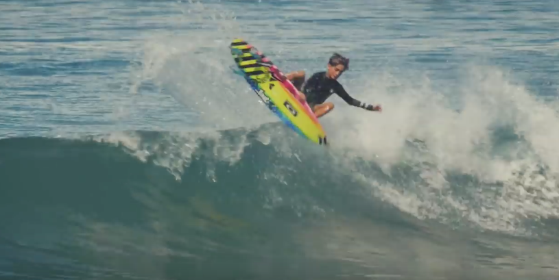 Surfer performing a trick on a wave with colorful board.