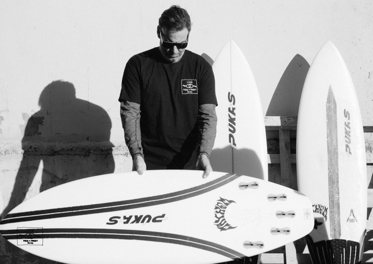 Man holding a surfboard with two others in the background.