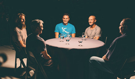 Five men seated around a round table with glasses of water.