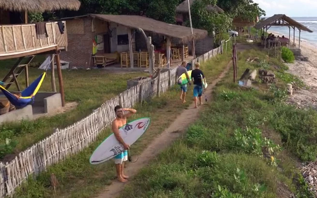 Surfers walking along a path near beachside huts.