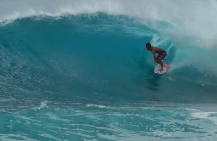 Surfer riding a wave inside a turquoise barrel.