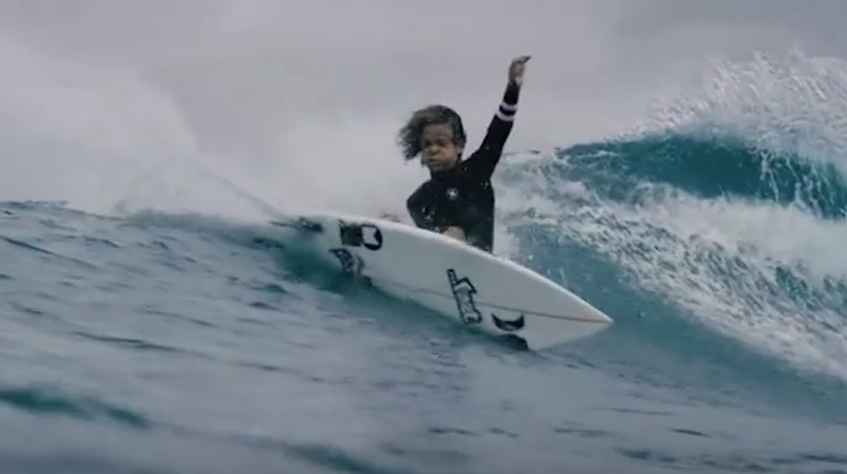 Child surfing on a wave, raising one arm in excitement.