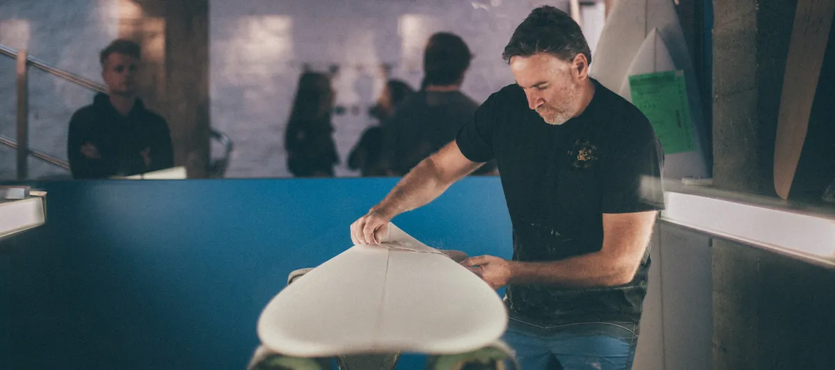 Man shaping a surfboard at a surf club event.