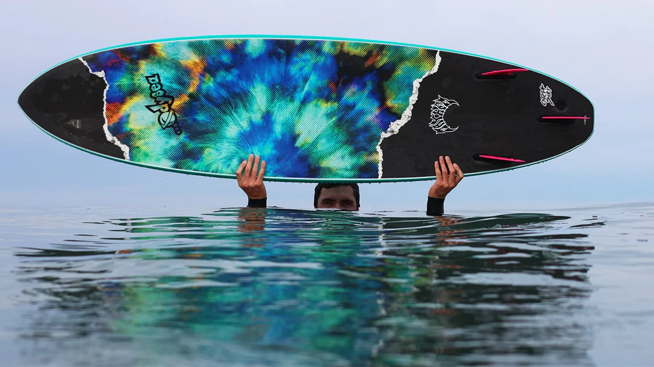 Person holding a colorful surfboard above water.